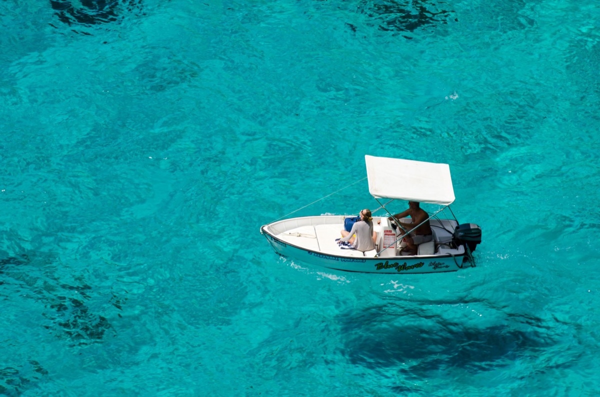 imbarcazione a motore con bandiera rosso e bianca in mezzo all'acqua turquoise a luce dorata